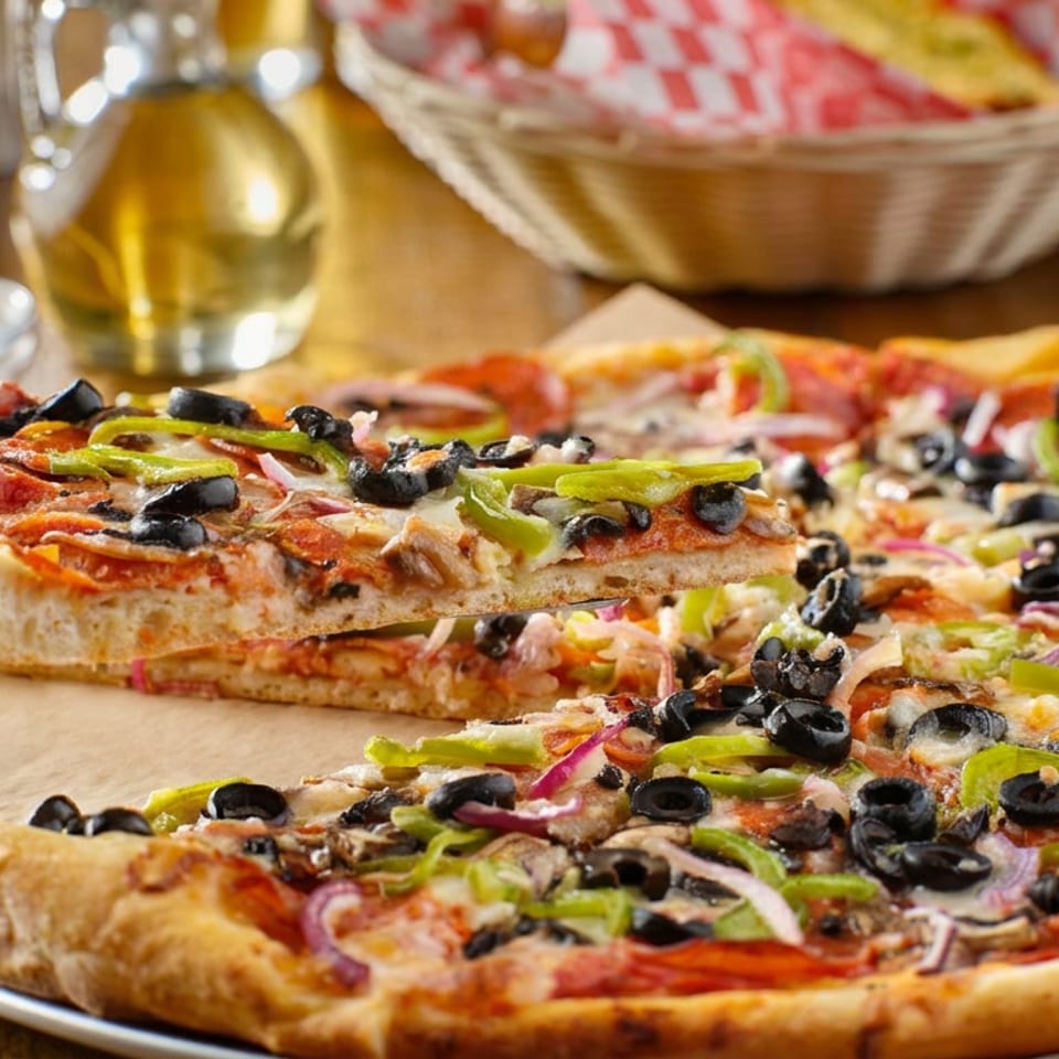 Two vegetable pizzas topped with black olives, green peppers, mushrooms, onions, and tomatoes on a wooden table.